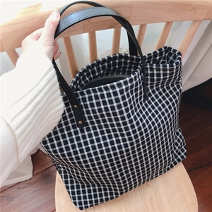 Close-up of black and white checkered tote bag featuring leather handles with metal rivets
