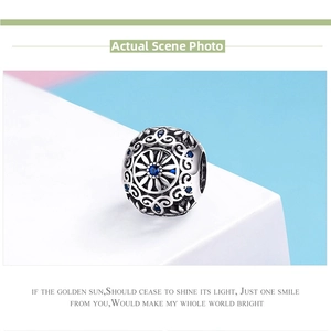 Macro detail of silver openwork charm bead with floral patterns and blue crystals