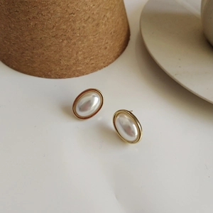 Close-up of vintage oval pearl earrings with gold plating on minimalist ceramic surface