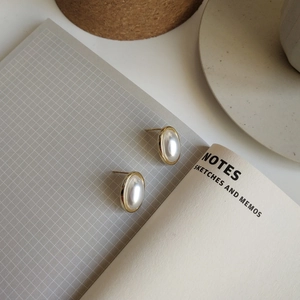 Detail of oval pearl stud earrings with light gold plating on a textured background