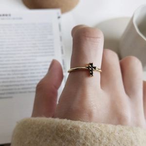 Detail of a minimalist gold ring with a black cross gemstone on a finger in soft lighting