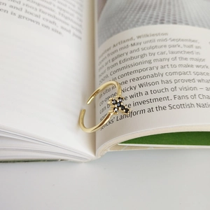 Close-up of gold cross open ring with black pavé stones on a lifestyle book background