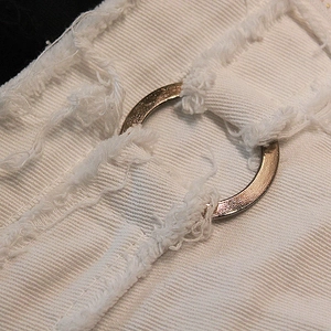 Dettaglio macro di pantaloncini di jeans bianchi con bordi sfilacciati e occhielli in metallo