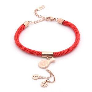 Macro detail of rose gold money bag charm and coin charms on red woven rope bracelet