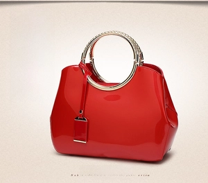 Detail of red patent leather bridal handbag featuring gold circular metal handle