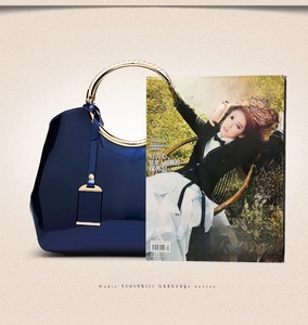 Detail of dark blue patent leather handbag next to a magazine for size reference