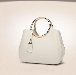 Detail of white patent leather handbag with gold ring handles and crocodile texture