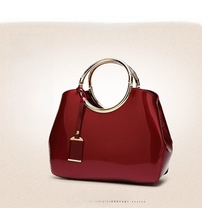 Detail of burgundy patent leather handbag with luxury gold circular metal handle