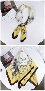 Macro detail of square silk scarf showing floral bird print and smooth satin texture