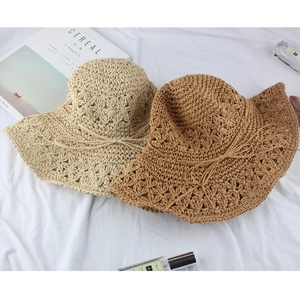Flat lay of woven straw sun hats with wavy brims in cream and brown on white fabric