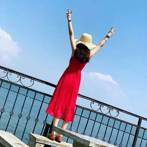 Red sleeveless dress with ruffle hem and straw hat set against a blue ocean background