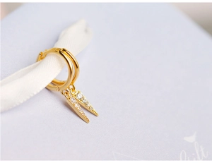 Detailed close-up of gold triangle hoop earrings with sparkling stones on a gift box