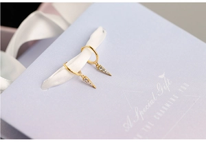 Detail of gold triangle earrings with clear zircons on a purple gift box