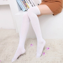 Detail of white over-the-knee socks worn by a model on a white plush rug for a cozy style