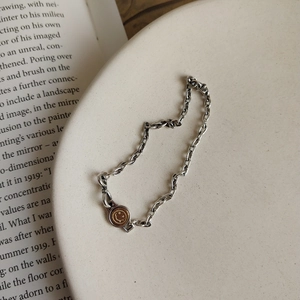 Detail of silver chain bracelet with golden smiley face pendant on a ceramic plate