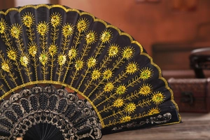 Detail of black folding fan featuring golden sequin floral embroidery and hollowed ribs