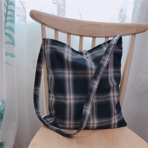 Détail d'un sac cabas en toile écossaise bleu et beige suspendu à une chaise en bois