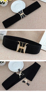 Detail view of black elastic corset belt featuring a gold buckle with black enamel inlay