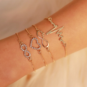 Close-up of four gold bracelets with heart, heartbeat, and infinity diamond charms