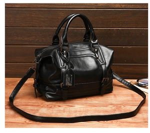 Classic black leather Boston bag with double handles and metallic hardware on wood desk