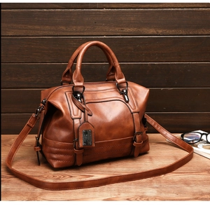 Close-up of brown Boston bag with decorative stitching, strap, and metal tag on wood