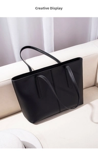 Close-up of a black matte leather tote bag with vertical stitching on a white sofa