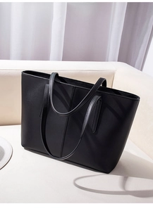 Minimalist black matte leather tote bag with vertical stitching on a light sofa
