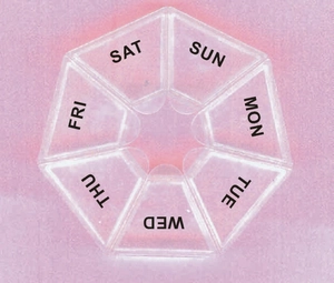 Close-up of a circular 7-compartment pill box with transparent lid and weekly day labels