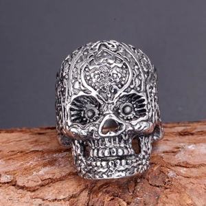 Close-up of vintage steel skull ring with intricate relief patterns on bark background