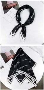 Detailed close-up of a black silk scarf with white geometric stripes and letter patterns