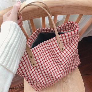 Close-up of red and white checkered canvas tote bag with leather straps on a chair