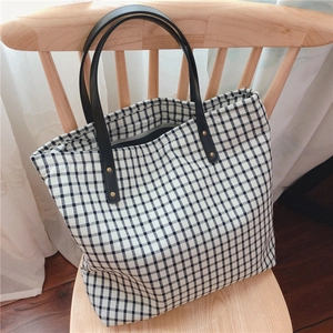 Detail of checkered canvas tote bag with black leather straps and gold rivets on a chair