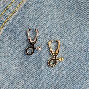 Creative stethoscope enamel brooches in gold and silver finish on denim background