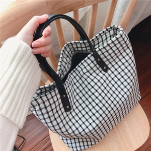 Close-up of black and white plaid tote bag with leather handles and gold metal rivets