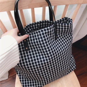 Detail of black and white checkered canvas tote bag with gold rivets and black straps
