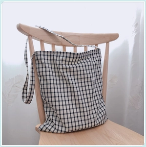 Détail d'un sac cabas en toile à carreaux vichy suspendu sur une chaise en bois clair