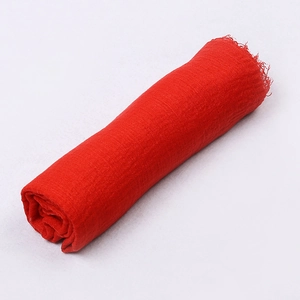 Detailed close-up of textured red crinkle scarf fabric with soft frayed edges on white