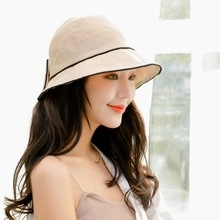 Detail view of a beige cotton sun hat with black contrast trim on the brim worn by a model