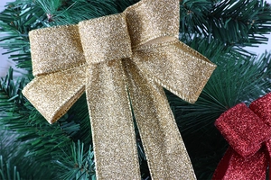 Close-up of glittery gold and red Christmas bows on a green pine branch background
