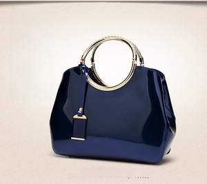 Detail of blue patent leather handbag with gold round metal handle and glossy finish
