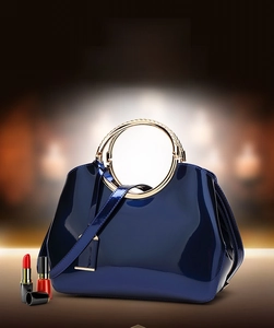 Detail of navy blue patent leather handbag with gold circular metal handles and strap