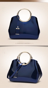 Detail of dark blue patent leather handbag with gold metal handle and crossbody strap