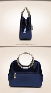 Detail view of dark blue patent leather bag with gold ring handle and zip pockets
