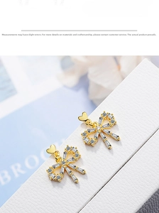 Close-up of gold bow earrings with crystal pave and delicate heart pendants