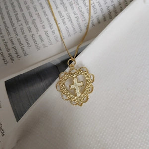 Macro shot of gold-plated heart pendant with cross inlay and beaded texture detail