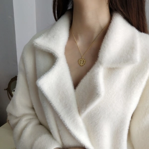 Detail of a gold cross heart pendant necklace worn by a model on a white fur coat