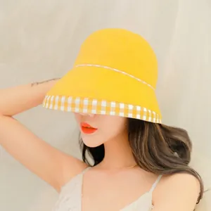 Detail of yellow cotton sun hat with gingham pattern brim worn by model outdoors