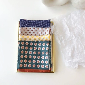 Close-up of four patterned silk pocket squares arranged in a gold-rimmed tray