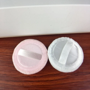 Detail of pink and white plush powder puffs with satin ribbons on a wooden surface