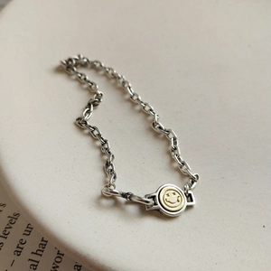 Minimalist 925 silver chain bracelet with a gold star-eye smiley pendant on ceramic plate